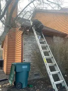 Technician cleaning gutters by hand, removing leaves and debris from a residential roofline.