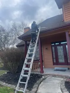 A Plus Home and Roof Wash technician on a ladder performing a pre-job roof inspection and taking photos at a home in Marion, Indiana