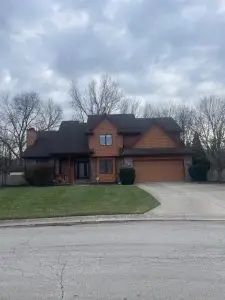 Home exterior before cleaning, showing dirty roof, clogged gutters, and stained driveway